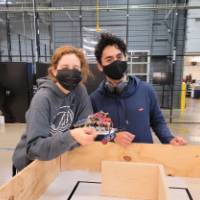 2 people holding a robot over a small maze